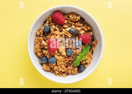 Homemade baked oat granola with fresh berries and raisins in bowl isolated on yellow background. Healthy breakfast cereals, dieting, clean eating conc Stock Photo