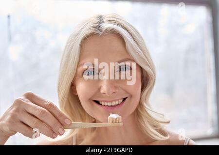 Happy smiling elderly woman portrait with bamboo toothbrush isolated on white. Stock Photo