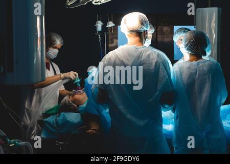 An international professional team of surgeon, assistants and anesthesiologist perform a complex operation on a patient under general anesthesia. Dark Stock Photo