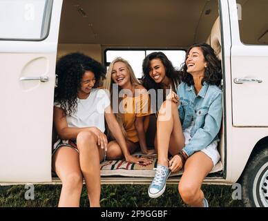 Multi ethnic group of women having fun while sitting in a car. Four friends traveling Stock Photo