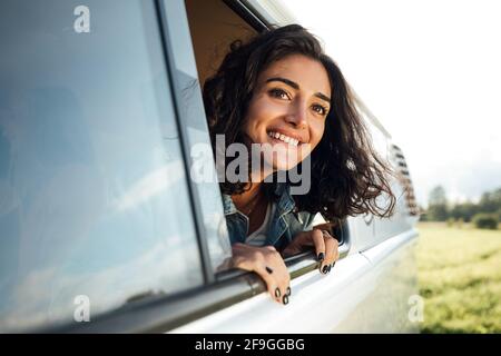 Beautiful brunette looks out of a window enjoying a road trip. Young woman in camper van Stock Photo