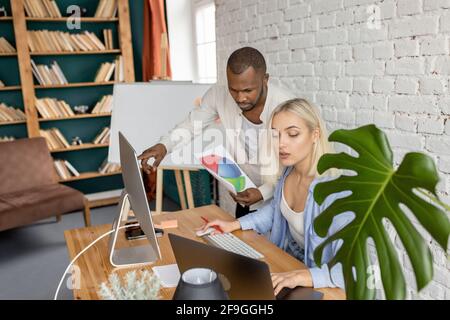 Focused serious employees learning financial graphs, working on important project. Multiracial coworkers discussing ideas for business strategy, using Stock Photo