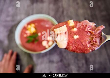 Spoon full of gazpacho cold soup with accompaniment ready to taste in focused close-up view, with bowl at the back out of focus. Point of view shot. C Stock Photo