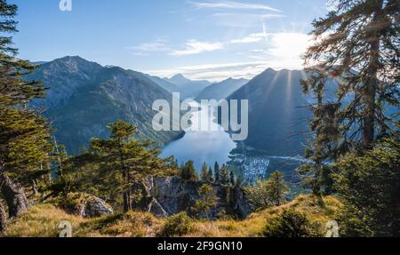 Hiking trail to Schoenjoechl, sun shining through light pine forest, Plansee with mountains, Tyrol, Austria Stock Photo