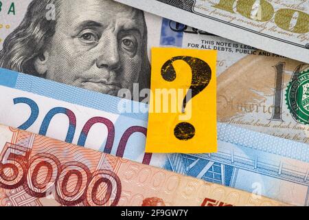 Russian rubles and one hundred dollar bills and a yellow paper note with a question mark on it. Closeup. Stock Photo