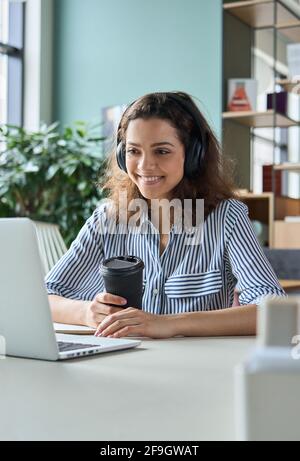 Young Hispanic female student in headphones talking online chat using laptop. Stock Photo