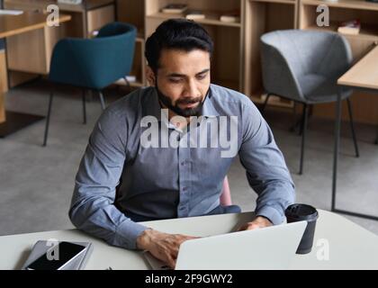 Serious indian business man working with laptop and cellphone in remote office. Stock Photo