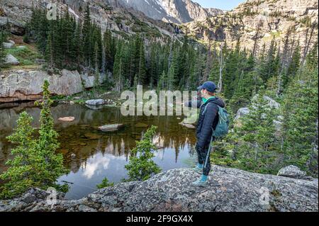 Hiker pointing down at the shallow Embryo Lake in the Loch Vale Stock Photo