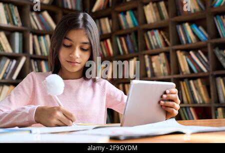 Concentrated latin schoolgirl watching online learning video at home on tablet. Stock Photo