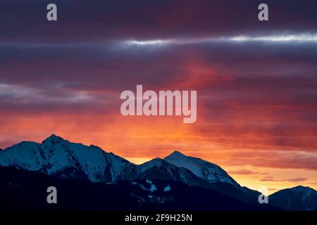 Rocky alpine mountain range during sunset with red orange illuminated clouds in Tirol, Austria Stock Photo
