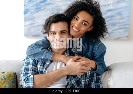 Portrait of a happy mixed race couple in love. Pretty african american curly girl and hispanic attractive guy tenderly hugging each other, looking at the camera, smiling, happy family Stock Photo