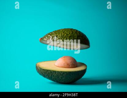 Floating avocado fruit sliced in half on aquamarine background. Minimal nature concept. Summer vibes. Healthy food idea. Stock Photo