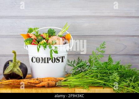 Kitchen compost bucket containing kitchen food waste with home grown vegetables on wooden board, recycle food waste by composting and growing your own Stock Photo