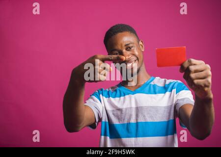 Portrait of an excited African man holding a credit card against a pink background Stock Photo