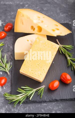 Various types of cheese with rosemary and tomatoes on black slate board on a black concrete background. Side view, close up, close up, selective focus Stock Photo