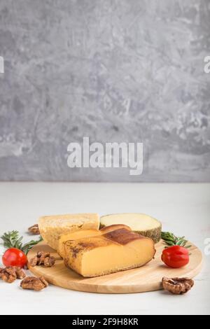 Smoked cheese and various types of cheese with rosemary and tomatoes on wooden board on a gray and white background. Side view, copy space, selective Stock Photo