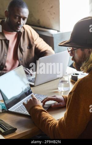Vertical portrait of two contemporary men using laptops while working at cafe table lit by sunlight in loft interior Stock Photo
