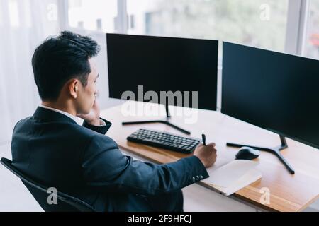 Asian business people are focused on working while on the phone. A computer with two blank screens Stock Photo