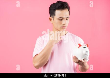 Young Asian man holding piggy bank on pink background Stock Photo