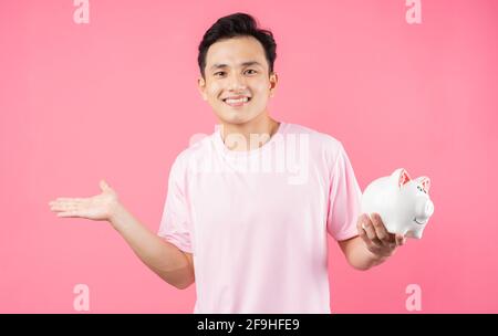 Young Asian man holding piggy bank on pink background Stock Photo