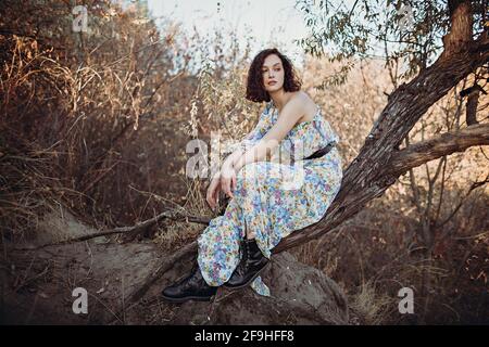 Young woman sits resting on leaning tree in autumn forest with her hands folded Stock Photo