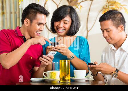 Asian people having fun together with mobile phone and drinking coffee or cocktail Stock Photo