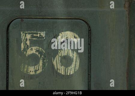 Number 56 painted on side of old rusted truck - number is white/cream colored, background is blue-green-grey Stock Photo