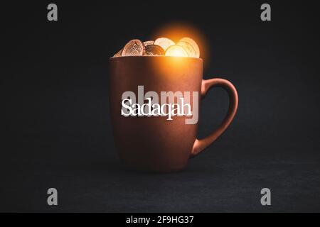 SADAQAH or Charity Gift text with Coins in cups on black background. Charity Concept Stock Photo