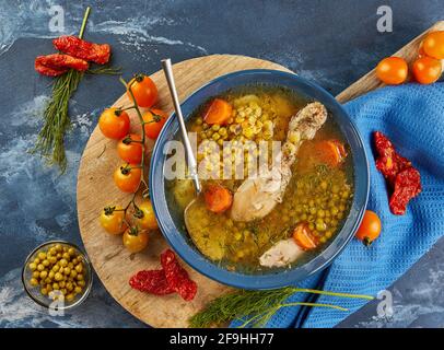 Pea soup with chicken, carrots, tomatoes and herbs in a deep plate on wooden board with napkin on blue background Stock Photo