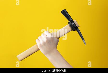 Close-up of pickaxe in man hand on yellow background. Advertising of tools for construction or dismantling. Poster for shop or necessary item for moun Stock Photo