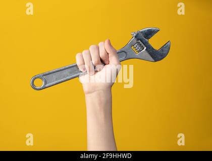 Close-up of large steel wrench in hand of man held up on yellow background. Tool for repair or construction. Symbol is ready to work or poster of  wor Stock Photo
