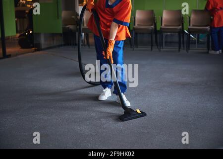Female janitor vacuuming the carpeted floor in the conference hall Stock Photo