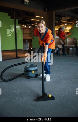 Smiling pretty cleaning lady vacuuming the floor Stock Photo