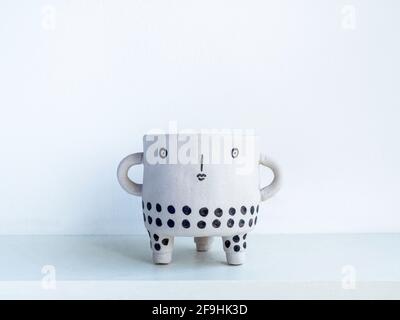 Empty cute face ceramic plant pot on white wooden shelf isolated on white wall background with copy space. Small modern DIY cement planter trendy deco Stock Photo
