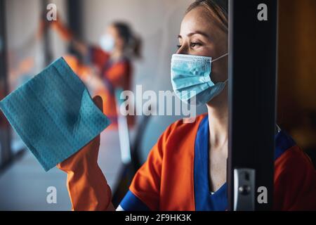 Pensive janitor in a disposable face mask doing the cleaning Stock Photo