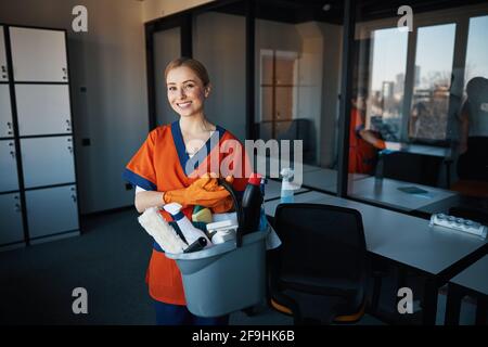 Pleased cleaning lady with janitorial supplies looking ahead Stock Photo