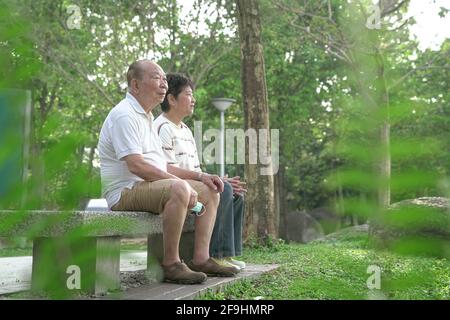 Senior Asian couple sitting on bench in the park. Copy space. Stock Photo