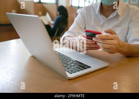 Man reading phone with computer laptop on table in a library. Close up shot. Stock Photo