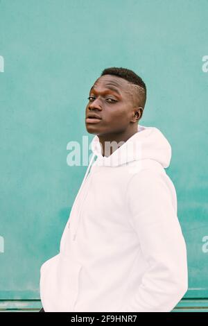 Young african black man against a green wall looking at camera wearing a white sweatshirt with style and confidence Stock Photo