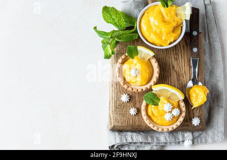 Lemon tartlets. Homemade shortbread mini tarts with lemon curd and meringue on wooden board, light concrete background. Top view. Selective focus. Stock Photo