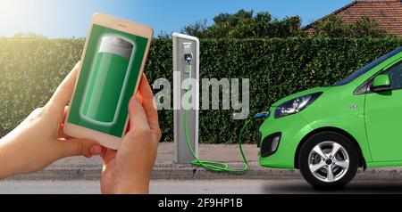 Hands with smartphone on a background of a car at the charging station for electric vehicles. Battery level on the phone screen Stock Photo