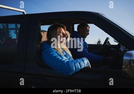 Man and woman in blue jackets sitting in car. Man trying to start engine of car, and woman looking wearily forward, leaning against the side door. Concept of travelling, car trip and relationships. Stock Photo