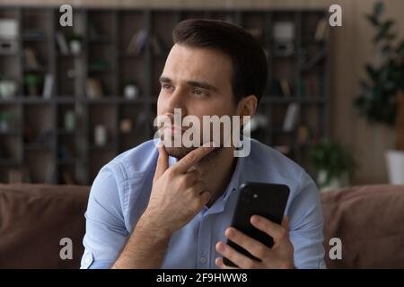 Pensive man use modern cellphone look in distance thinking Stock Photo