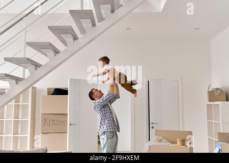 Happy young father playing lifting cute child son celebrating moving day. Stock Photo