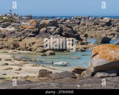 A small fishing boat at anchor in a cove on the rocky coast of northern Finistère in Brittany. In the distance the semaphore of Brignogan-Plage* Stock Photo