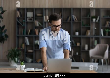 Successful man stand at desk working on laptop online Stock Photo