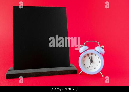 Wooden chalkboard mockup or wooden frame, alarm clock 12 hours on red surface. Dark information board template, sign board for menu in cafe Stock Photo