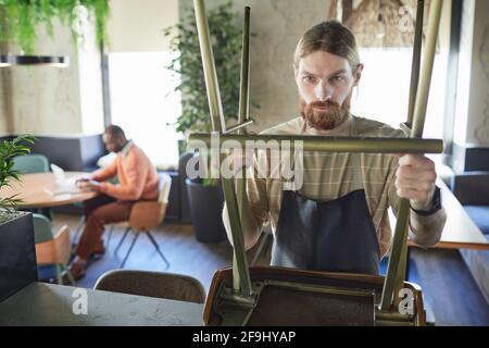 Waist up portrait of bearded cafe worker arranging furniture while preparing for opening in morning, copy space Stock Photo