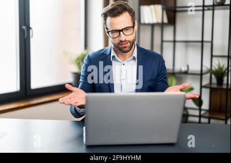 Slavic business man in stylish suit having virtual team meeting on video conference call using laptop work from home office talking to diverse group or colleague in remote online distance chat Stock Photo