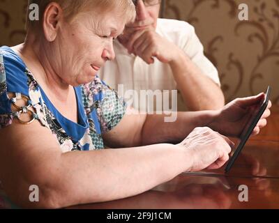 An elderly couple is sitting at a tablet and looking for information on the Internet Stock Photo